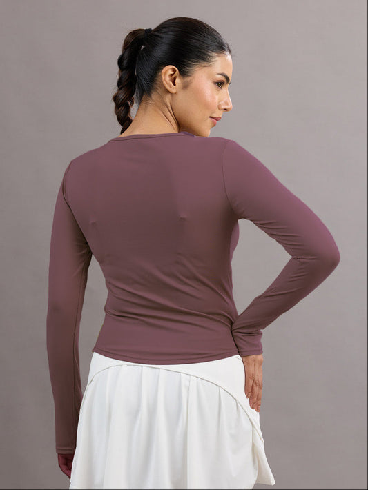 Woman wearing a long-sleeve mauve top and white skirt against a gray background