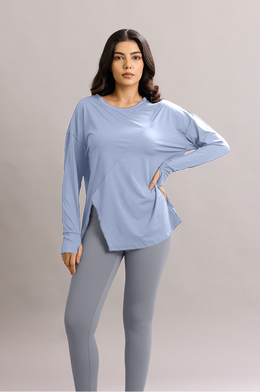 Woman wearing a light blue long-sleeve top and gray leggings on a plain background