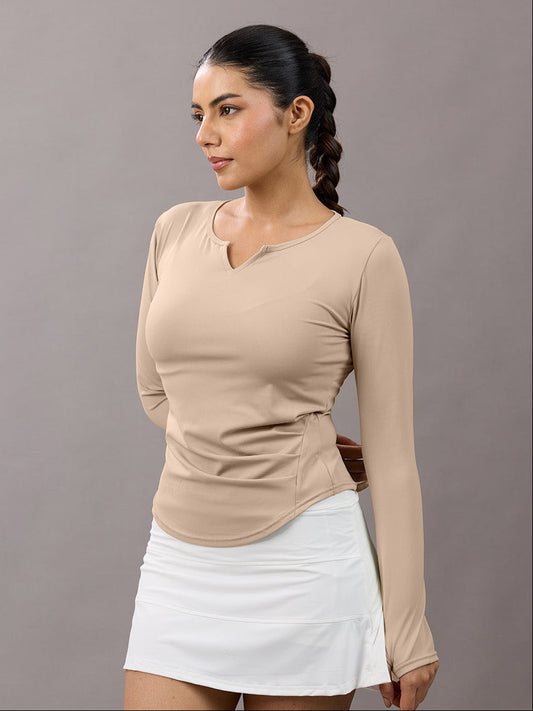 Woman wearing a beige long-sleeve top and white skirt against a gray background