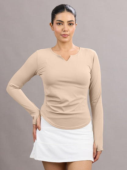 Woman wearing a beige long-sleeve top and white skirt against a gray background