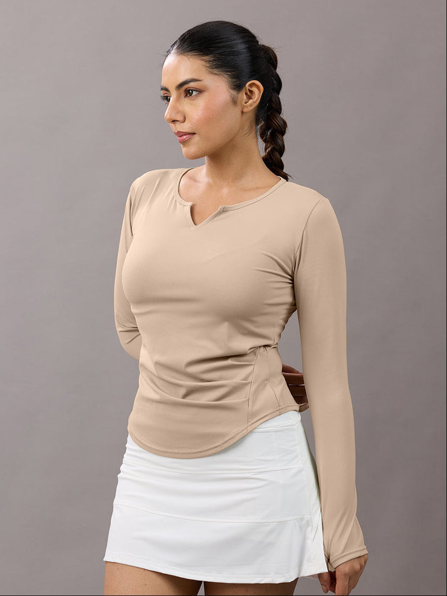 Woman wearing a beige long-sleeve top and white skirt against a gray background
