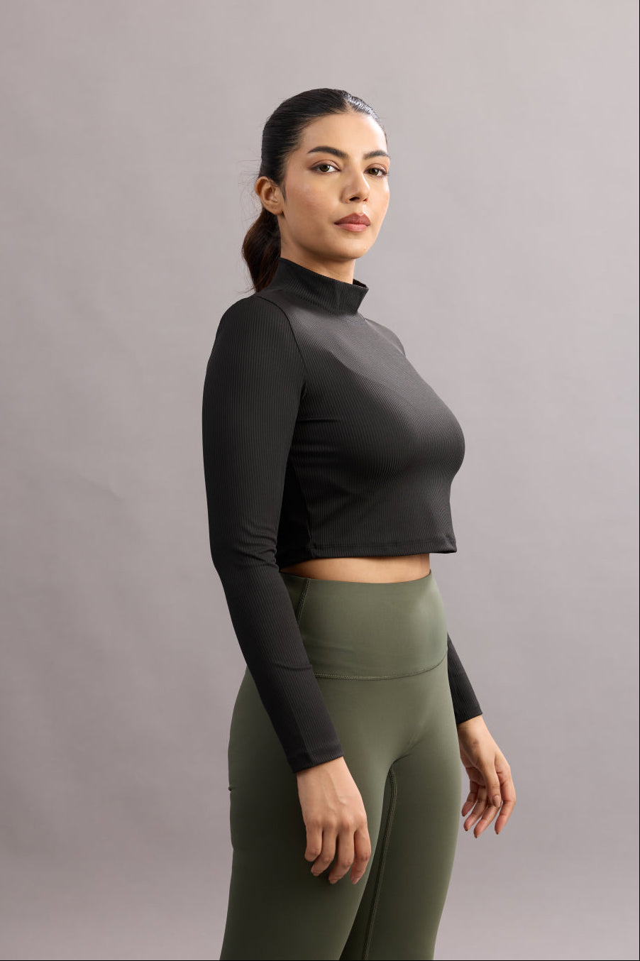 Woman wearing a black long-sleeve top and green leggings against a gray background