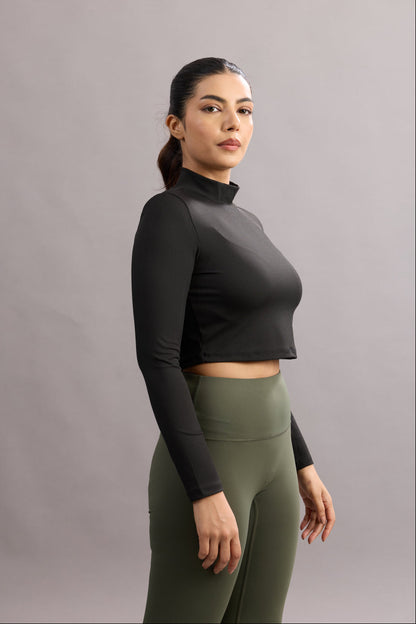 Woman wearing a black long-sleeve top and green leggings against a gray background