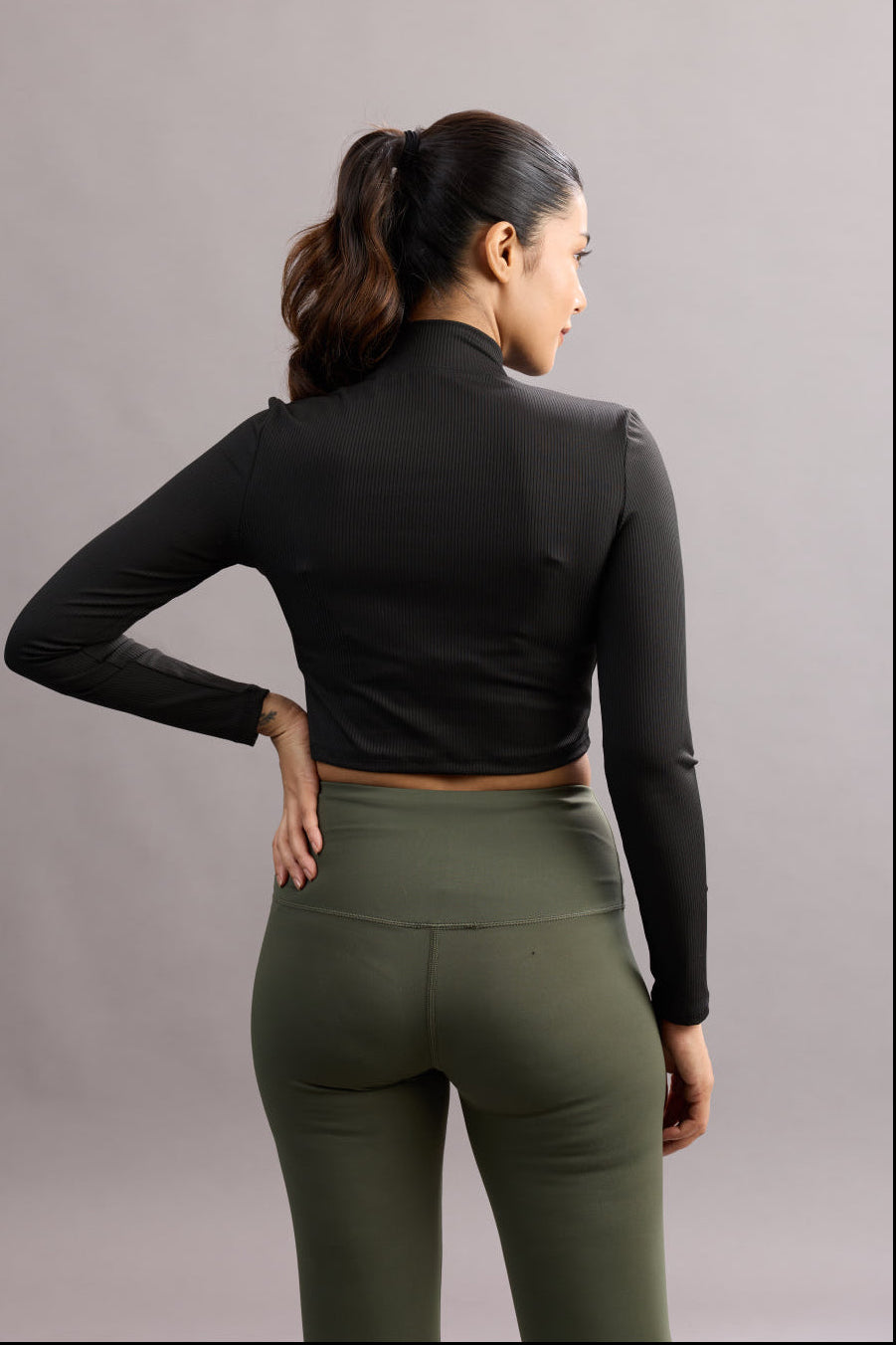 Woman wearing a black long-sleeve crop top and green leggings against a gray background