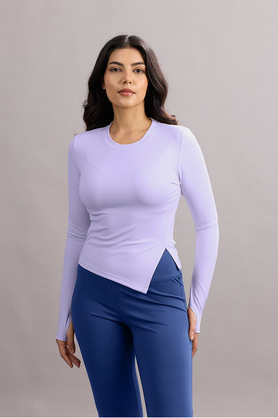 Woman wearing a light purple long-sleeve top and blue leggings against a gray background
