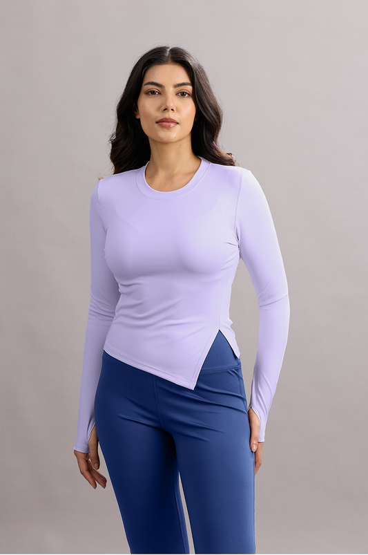 Woman wearing a light purple long-sleeve top and blue leggings against a gray background