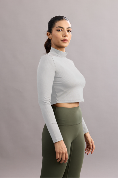 Woman wearing a white long-sleeve crop top and green leggings against a plain background