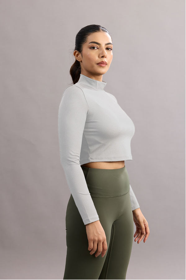 Woman wearing a white long-sleeve crop top and green leggings against a plain background