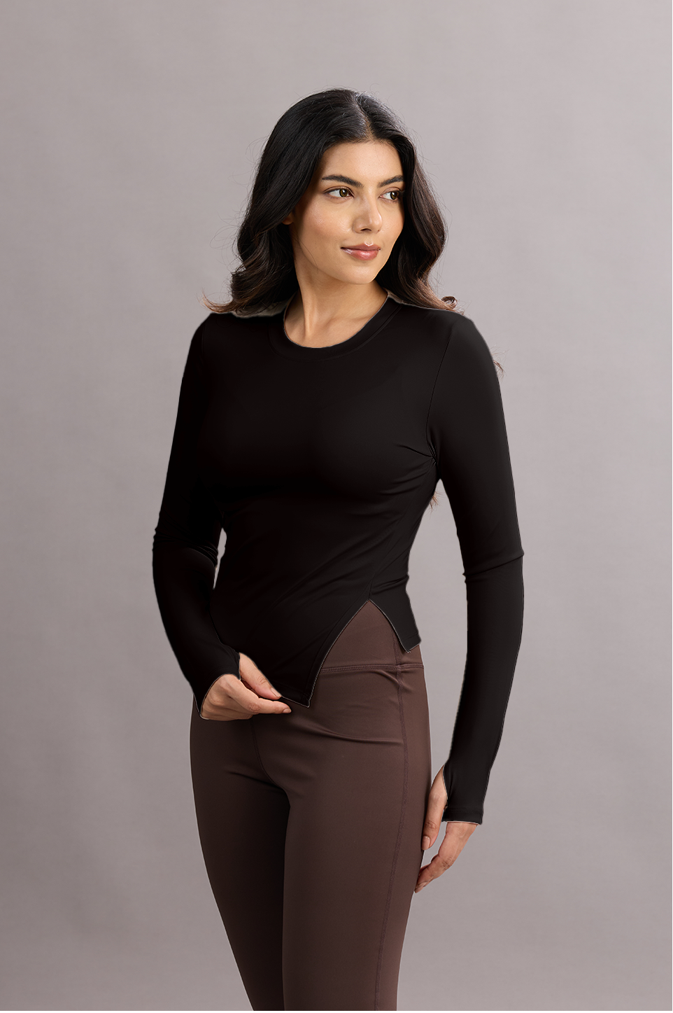 Woman wearing a black long-sleeve top and brown pants against a gray background
