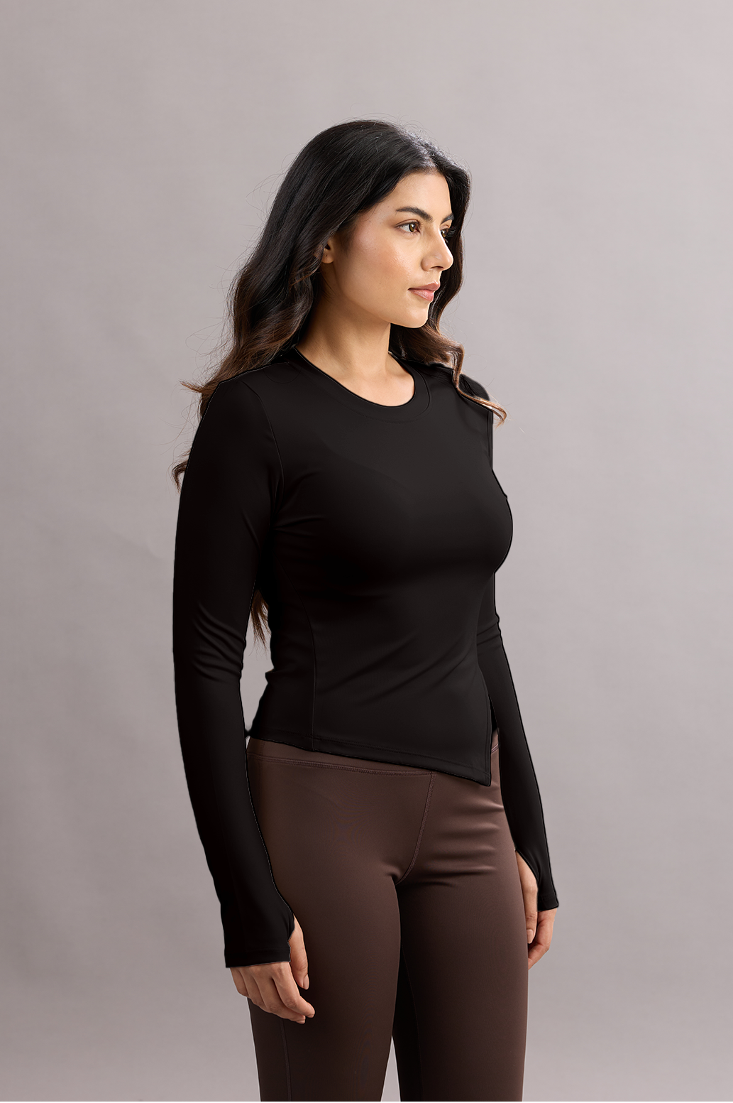Woman wearing a black long-sleeve top and brown pants against a gray background